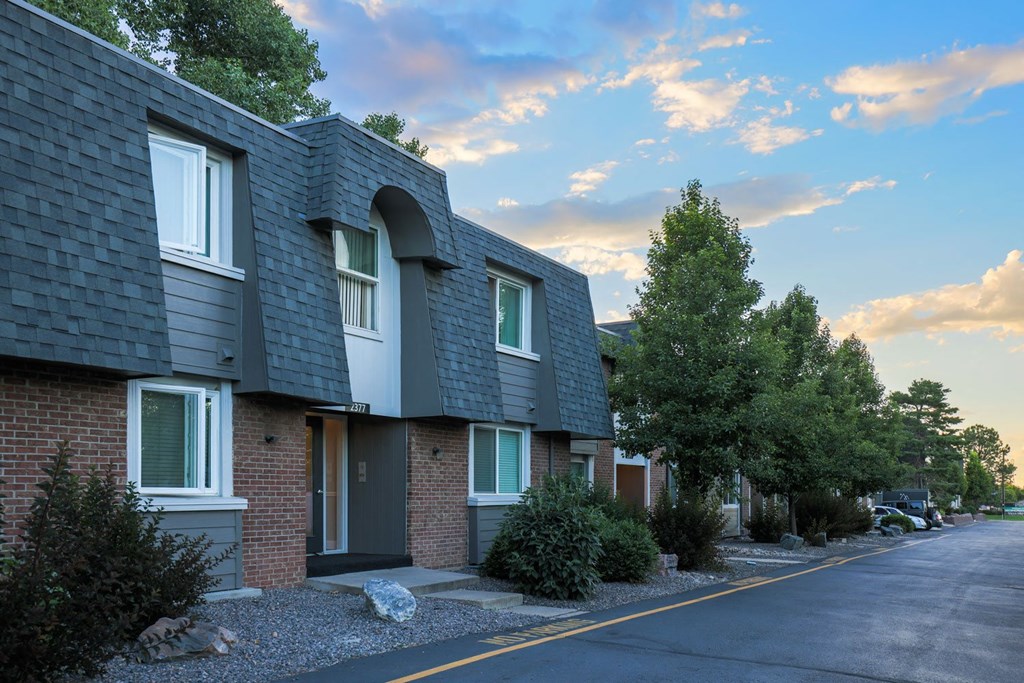 a street in front of a brick apartment building with a cloudy sky