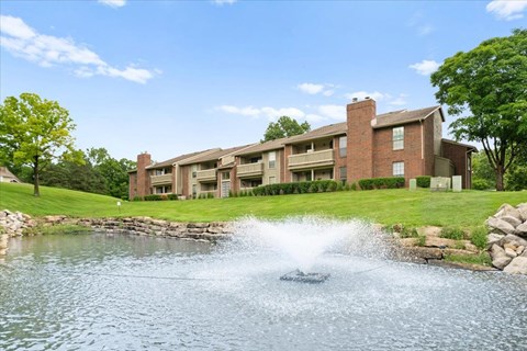 A fountain in the middle of a pond in front of a building.