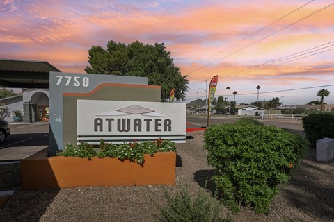 Apartment community entrance sign displaying 'Atwater' with landscaped shrubs and a colorful sunset sky in the background.