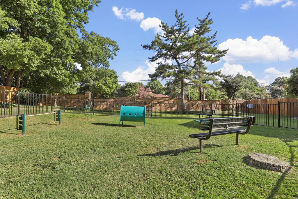 A park with a bench, trees, and a fence.