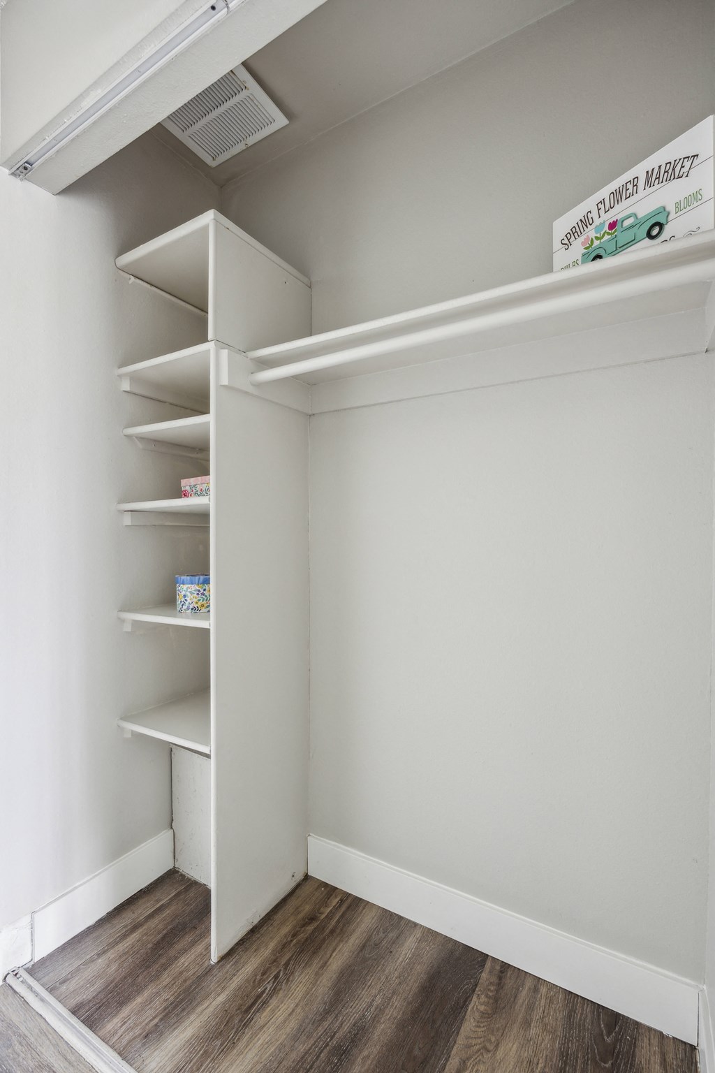 a walk in closet with white walls and shelves and a wood floor