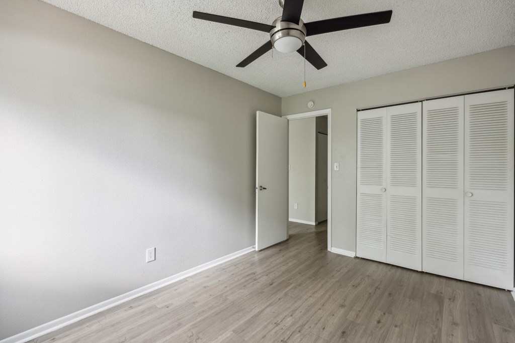 an empty living room with a ceiling fan and a closet