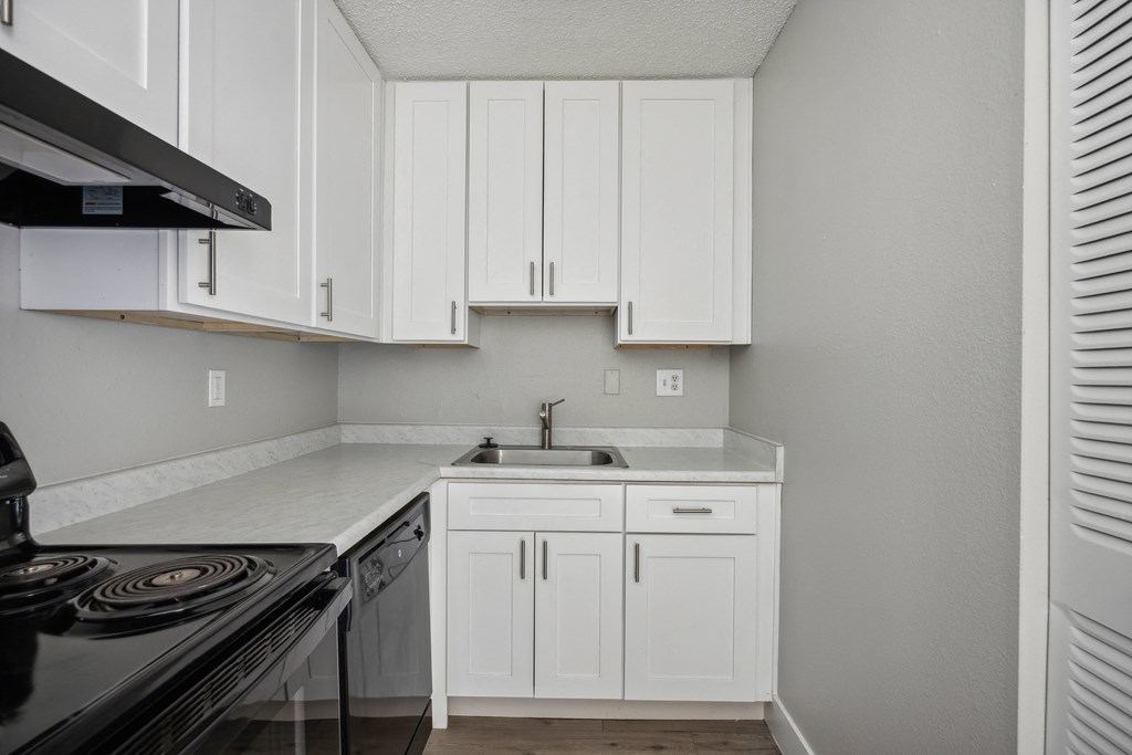 an empty kitchen with white cabinets and a stove and sink