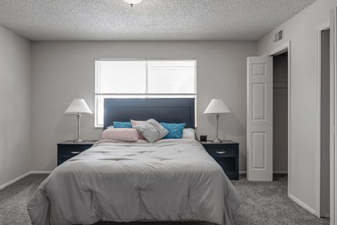 A bedroom with a bed, two lamps, and a window.