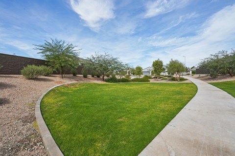 A curved concrete pathway leads through a grassy area with trees.