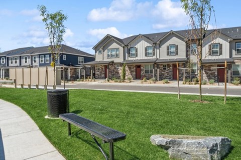 A park with a bench and a trash can in front of apartment buildings.