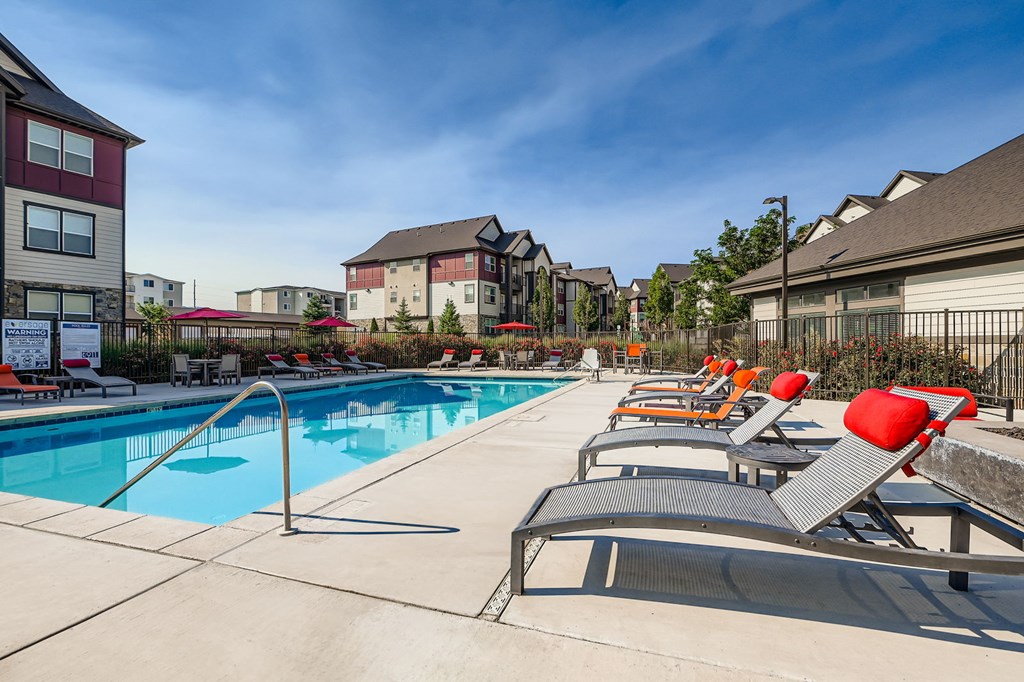 A swimming pool with red chairs and apartment buildings in the background.