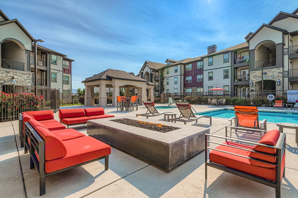 A pool area with red chairs and a fire pit in front of apartment buildings.