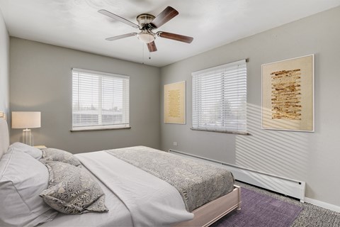 A bedroom with a bed, a ceiling fan, and two framed pieces of artwork on the wall.