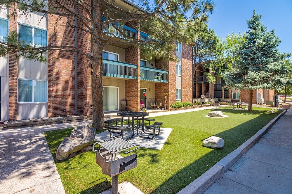 A sunny day at a brick apartment complex with a green lawn and trees.