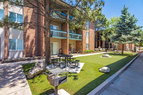 A sunny day at a brick apartment complex with a green lawn and trees.