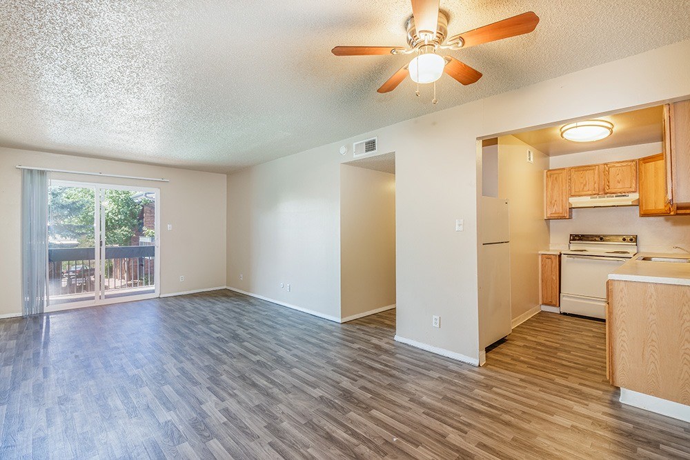 A room with a ceiling fan and a kitchen area in the background.