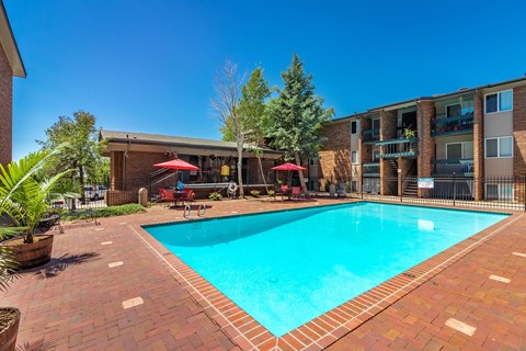 A swimming pool surrounded by a brick patio and a building in the background.