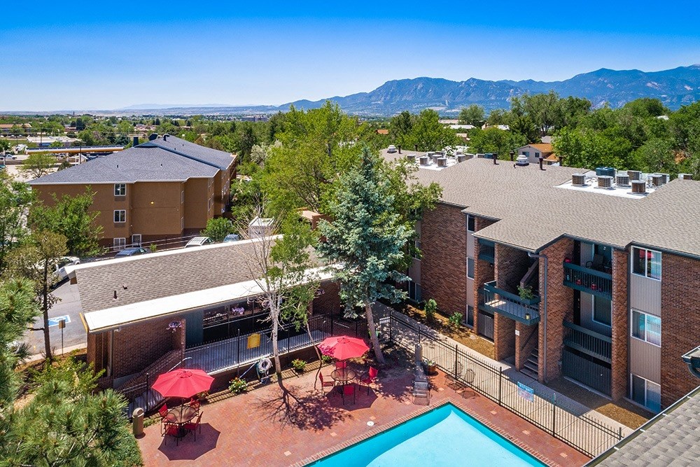A pool surrounded by a red umbrella and chairs.