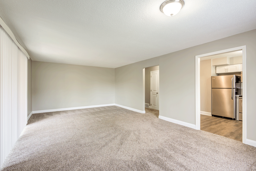 an empty living room with a stainless steel refrigerator