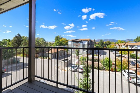 A balcony with a black railing overlooks a parking lot and buildings.