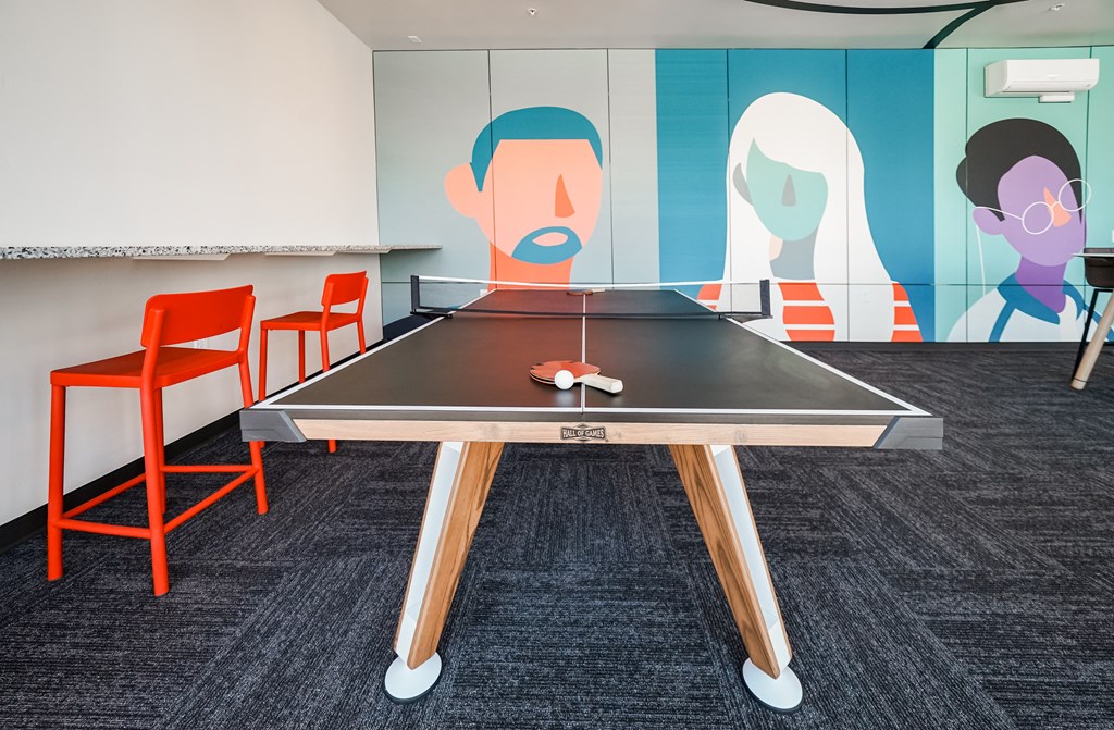 a ping pong table in a room with orange chairs and a wall with paintings