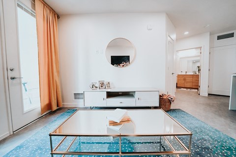 a living room with a glass coffee table and a mirror