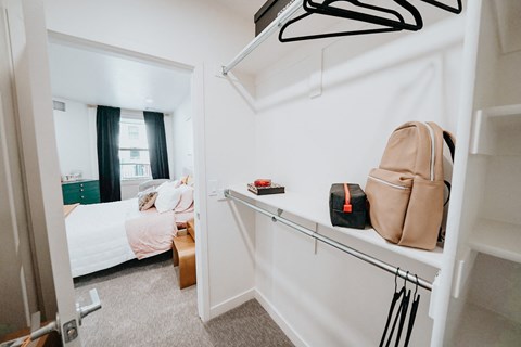 a bedroom with a bed and a closet with purses and bags on a wall