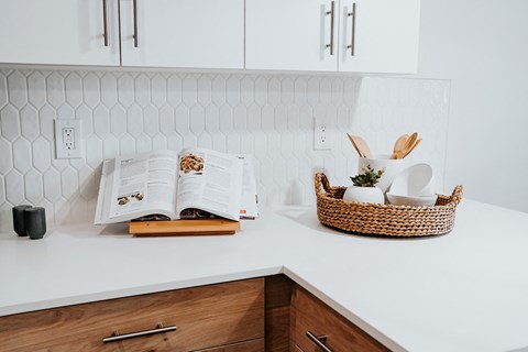 a white kitchen counter with a basket and an open book on it