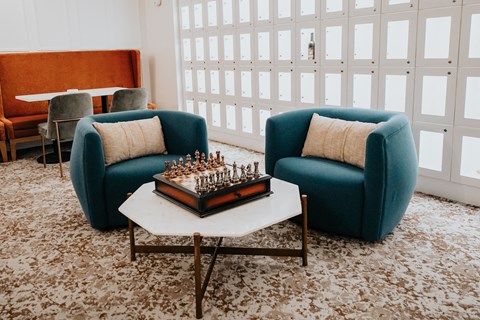 a living room with two blue chairs and a coffee table with a chess board