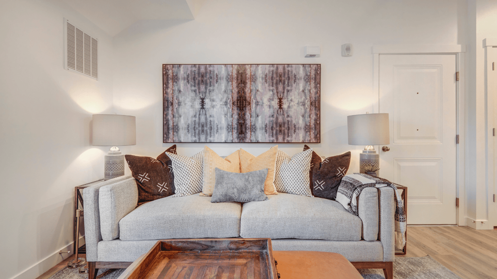 A living room with a grey couch and a large abstract painting on the wall.