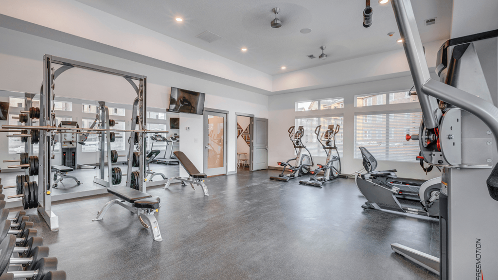 A spacious gym with a variety of equipment including a treadmill, weights, and exercise bikes.