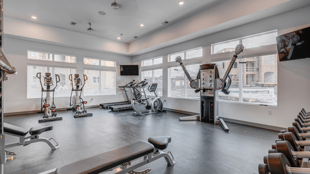 A well-equipped gym with various exercise machines and a flat screen TV mounted on the wall.