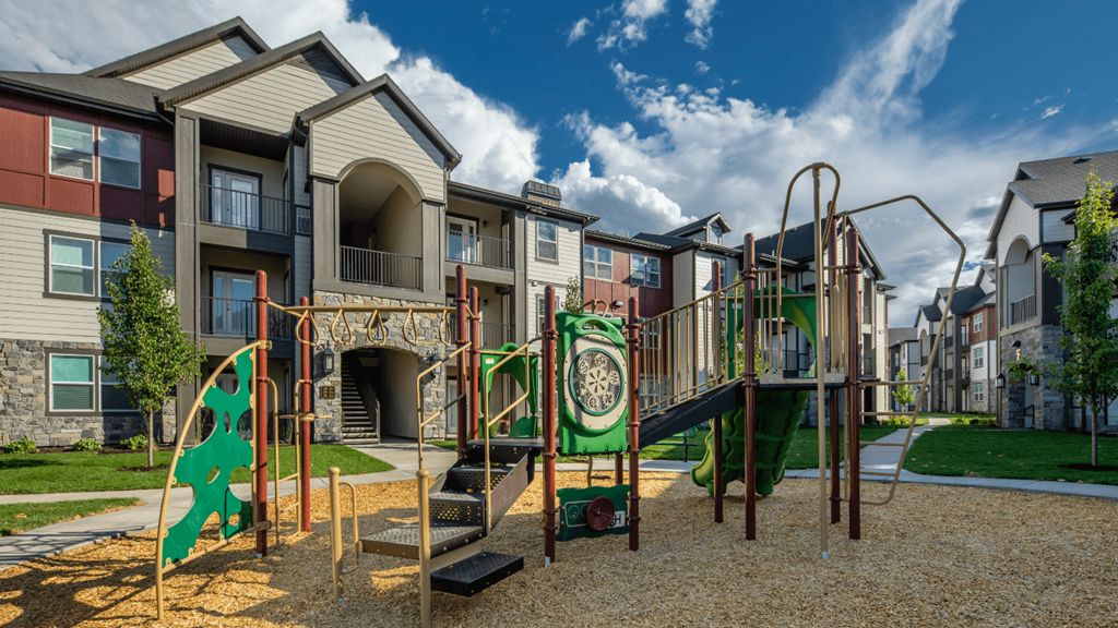 A playground with a green slide and a play structure in front of apartment buildings.