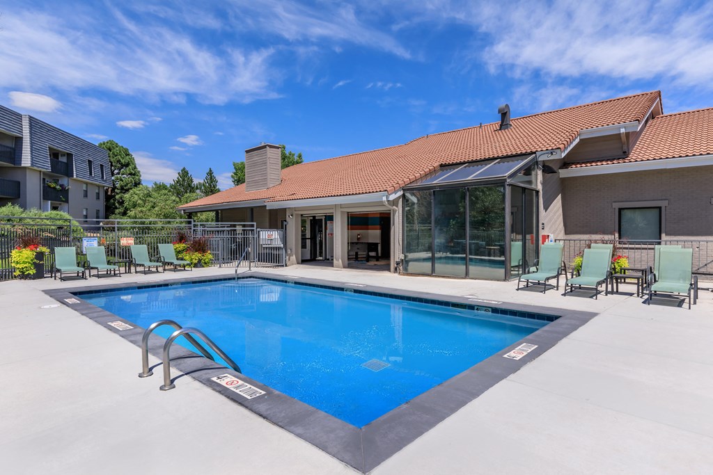 A large swimming pool in front of a house with a patio and lounge chairs.