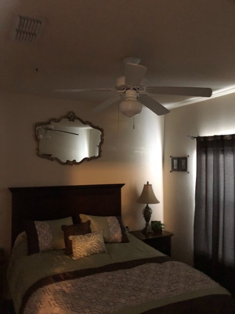 A bedroom with a bed, a ceiling fan, and a mirror.