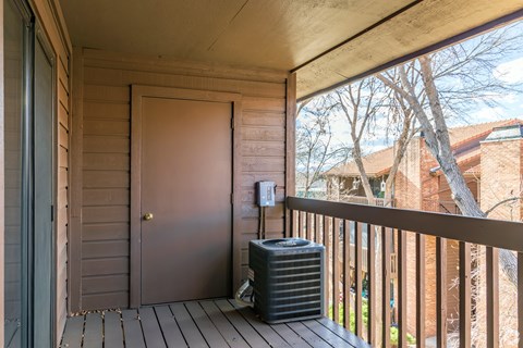 A black air conditioning unit sits on a wooden deck.