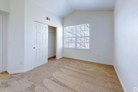 A room with a carpeted floor and a window with a view of a building.