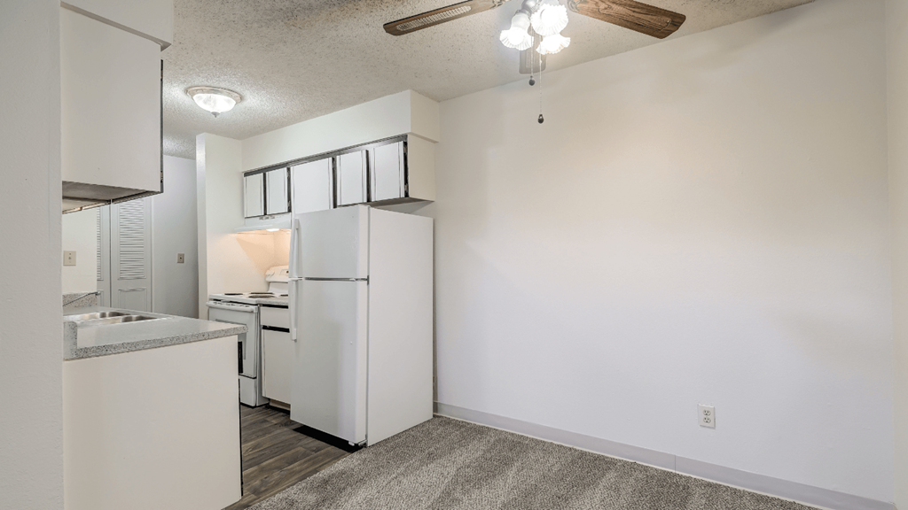 the living room and kitchen of an apartment with white cabinets and a white refrigerator