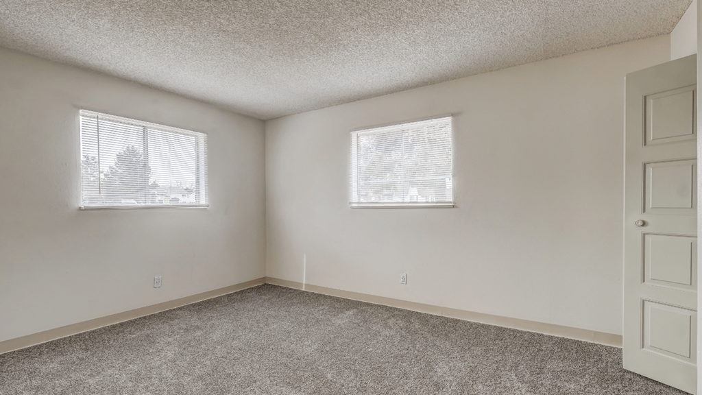 an empty bedroom with two windows and a door