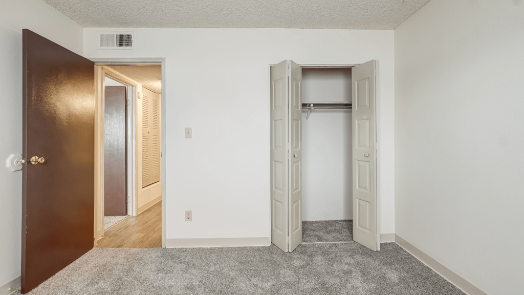 an empty room with a door to a closet and a hallway with an open door
