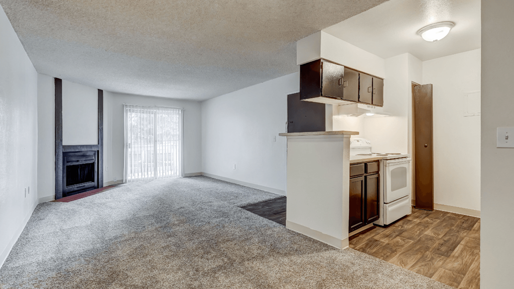 an empty living room with a kitchen and a fireplace