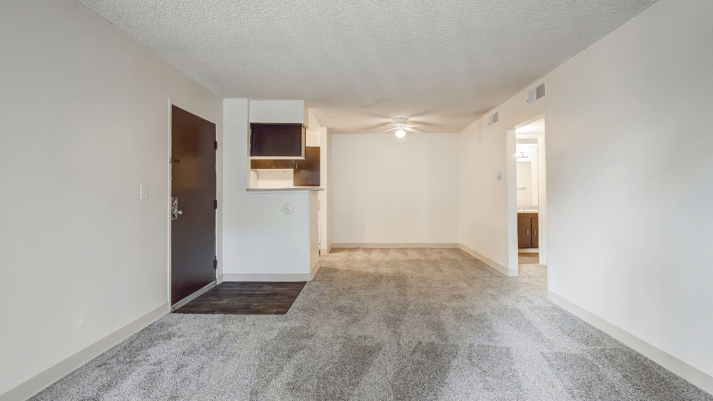 an empty living room and kitchen with white walls and carpeting
