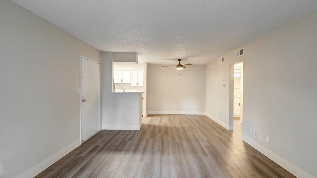 an empty living room and kitchen with hardwood floors and a ceiling fan