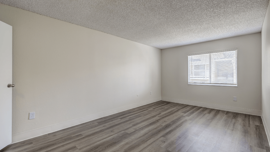 an empty bedroom with hardwood flooring and a window