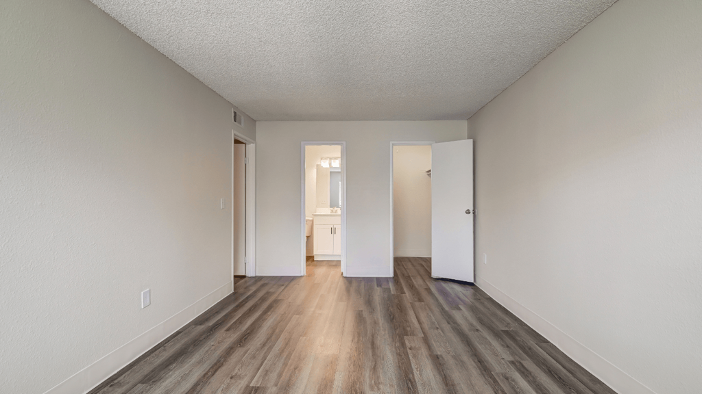 the spacious living room of an apartment with wood flooring and white walls