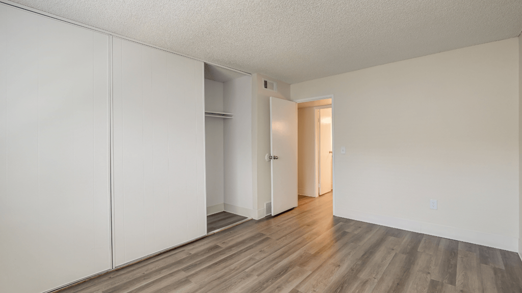 an empty bedroom with white walls and wood flooring