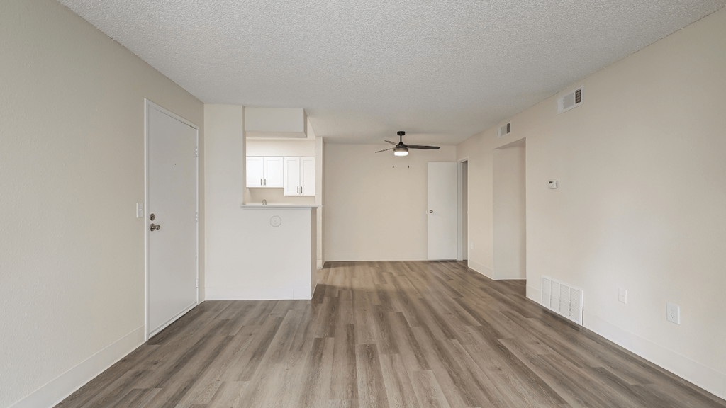 an empty living room and kitchen with white walls and wood flooring