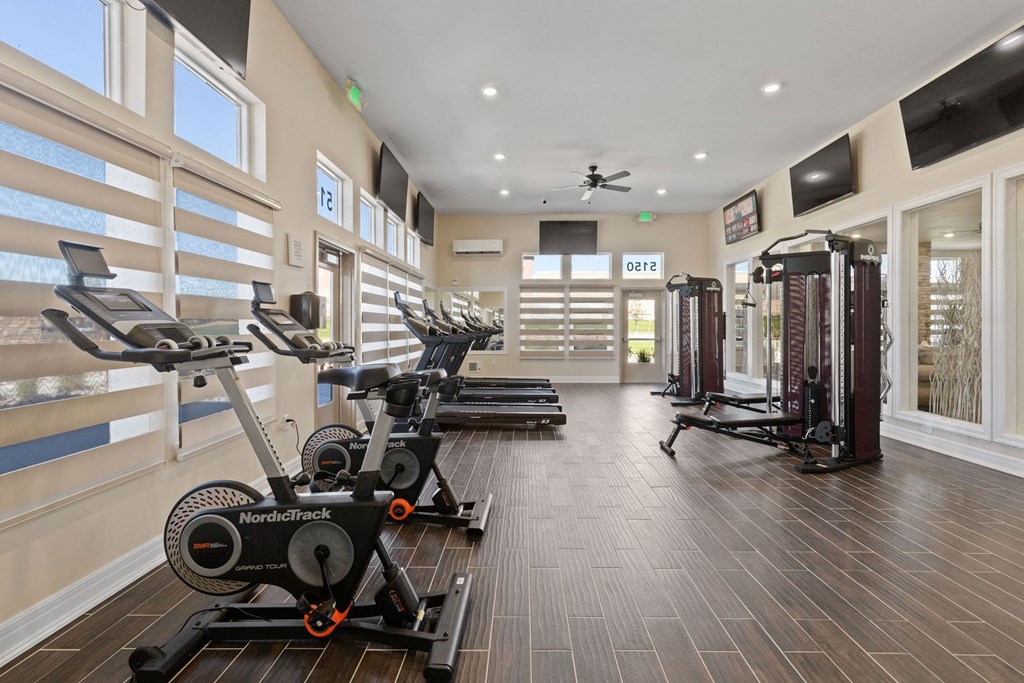 a gym with weights and cardio equipment in a building with large windows