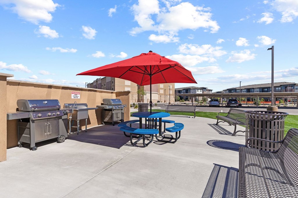 a patio with a red umbrella and tables with chairs and a grill