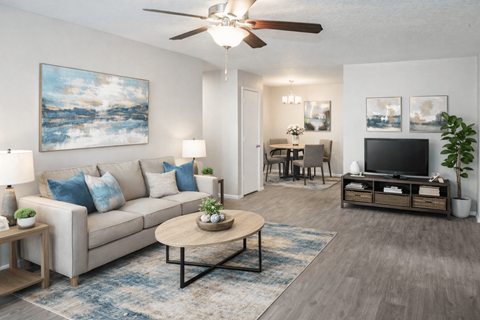 A living room with a beige couch, a coffee table, a ceiling fan, and a painting on the wall.