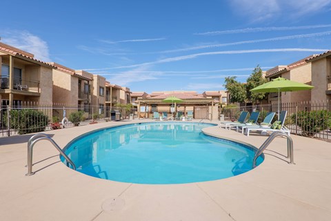 A swimming pool in a residential area with sun loungers and umbrellas.