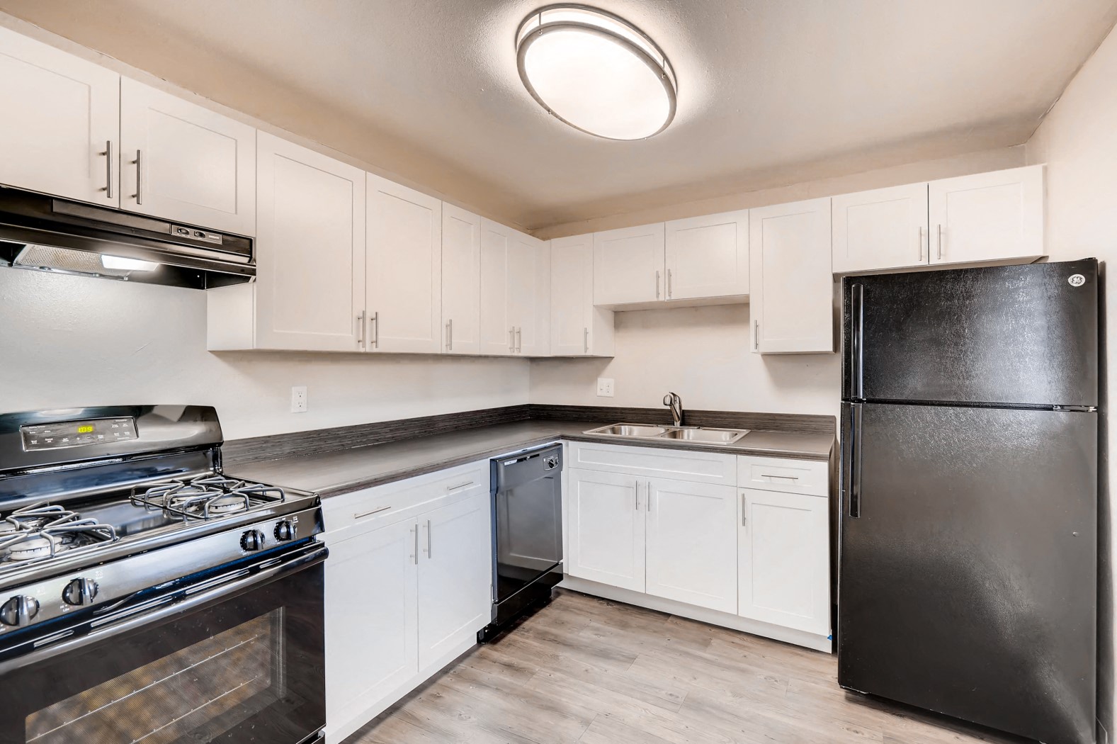 A kitchen with white cabinets and a black refrigerator.
