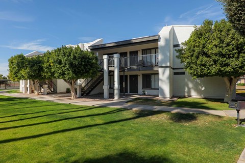 A white building with a balcony and a tree in front.