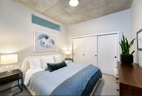 A bedroom with a bed, nightstand, and a plant.